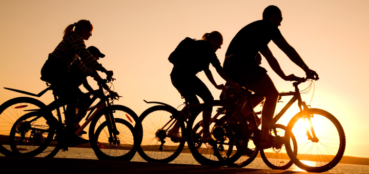 Image of sporty company friends on bicycles outdoors against sunset. Silhouette